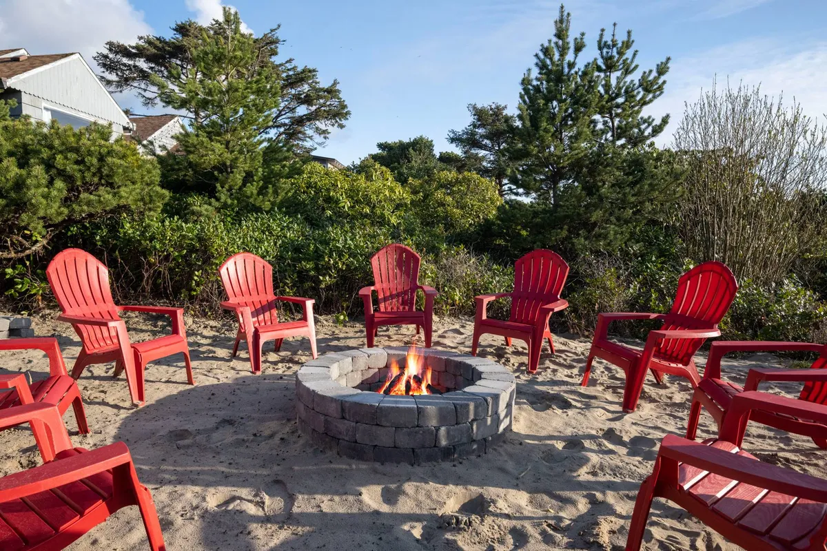 An inviting backyard fire pit scene with bright red chairs surrounded by lush greenery, creating a cozy spot for gatherings, relaxation, and enjoying sunsets after a day at the beach.