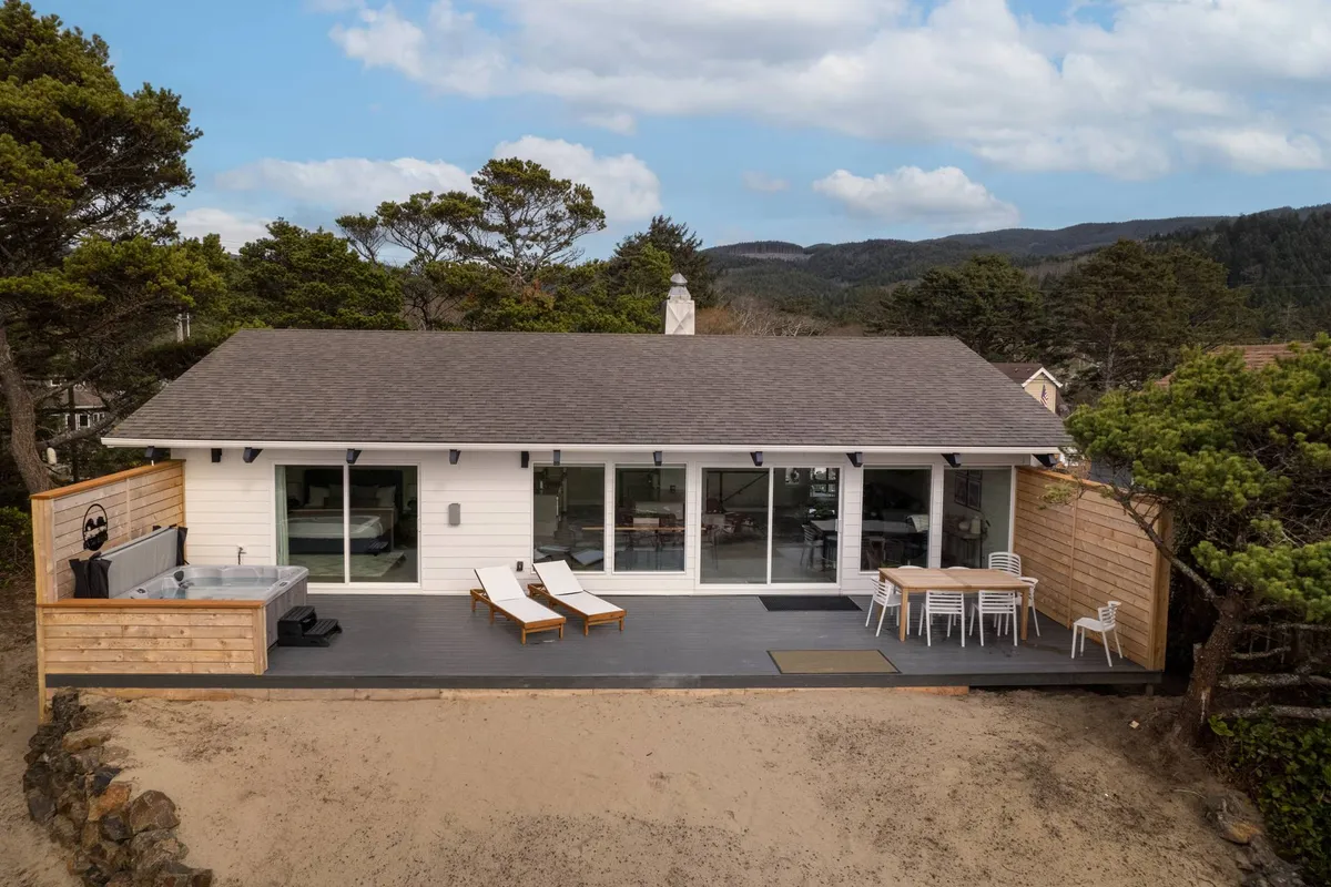The house exterior featuring a spacious deck with outdoor furniture and a hot tub, set against a backdrop of greenery with the beach just beyond. This scene suggests easy transitions from indoor comforts to outdoor fun and relaxation.