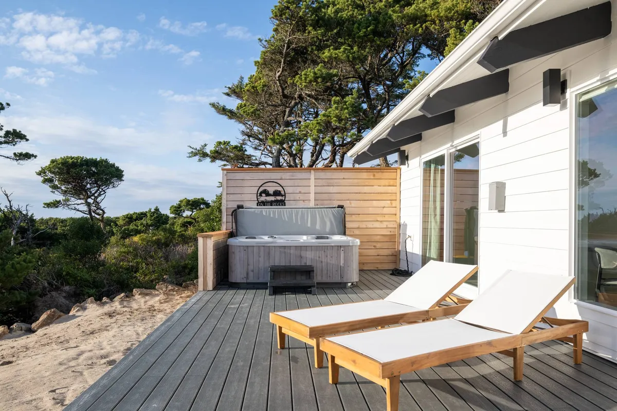 The wooden deck is featured with a bubbling hot tub, lounge chairs, and lush surrounding trees. The setting is tranquil, perfect for soaking and unwinding while being bordered by nature.