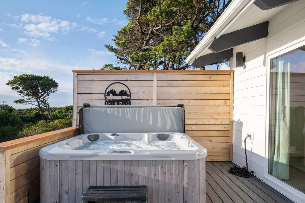 This image shows a tranquil outdoor hot tub surrounded by lush greenery and a wooden privacy wall. The setting is both intimate and inviting, perfect for unwinding after a day of coastal exploration. The ambiance suggests relaxation and privacy, ideal for couples or friends sharing special moments.