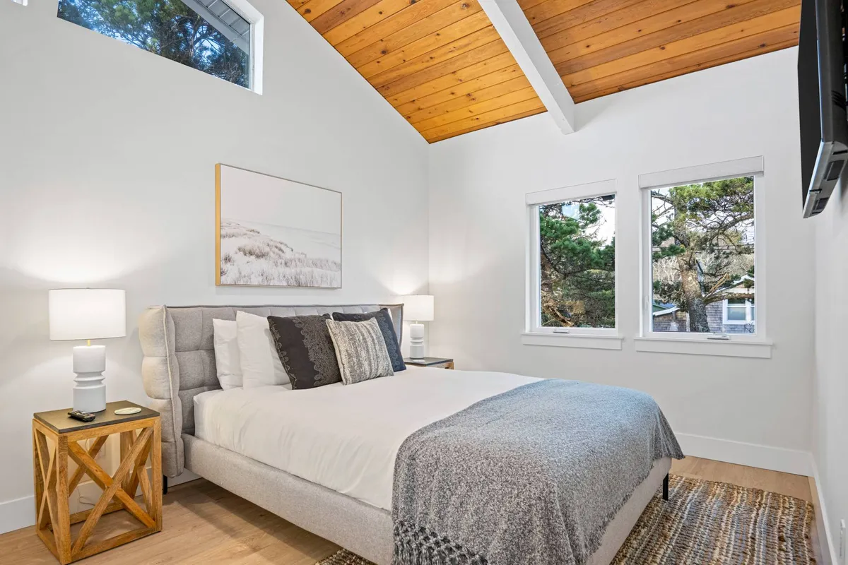A cozy bedroom with a comfortable bed, warm lighting from bedside lamps, and large windows that invite sunlight. Tasteful artwork accents the calming atmosphere, making it an inviting spot to relax and unwind.