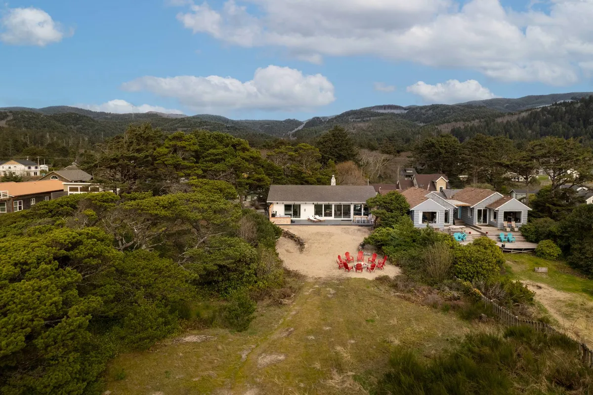 A serene outdoor scene with green trees, beach houses, and red chairs arranged for relaxation. This setup hints at moments spent watching the sunset, gathering by a fire, or stargazing—all with the beach close at hand.